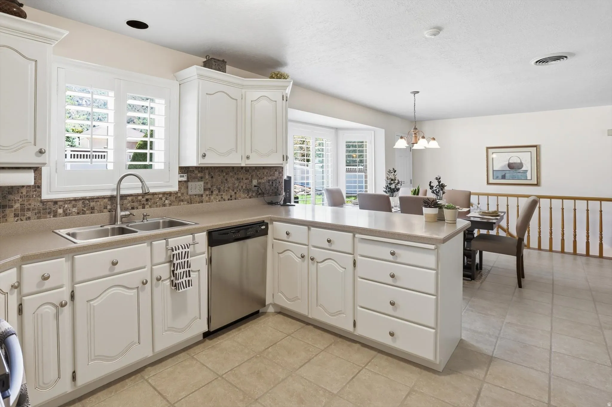 Kitchen featuring white cabinetry, light-toned countertops, a stainless steel double sink, and a stainless steel dishwasher