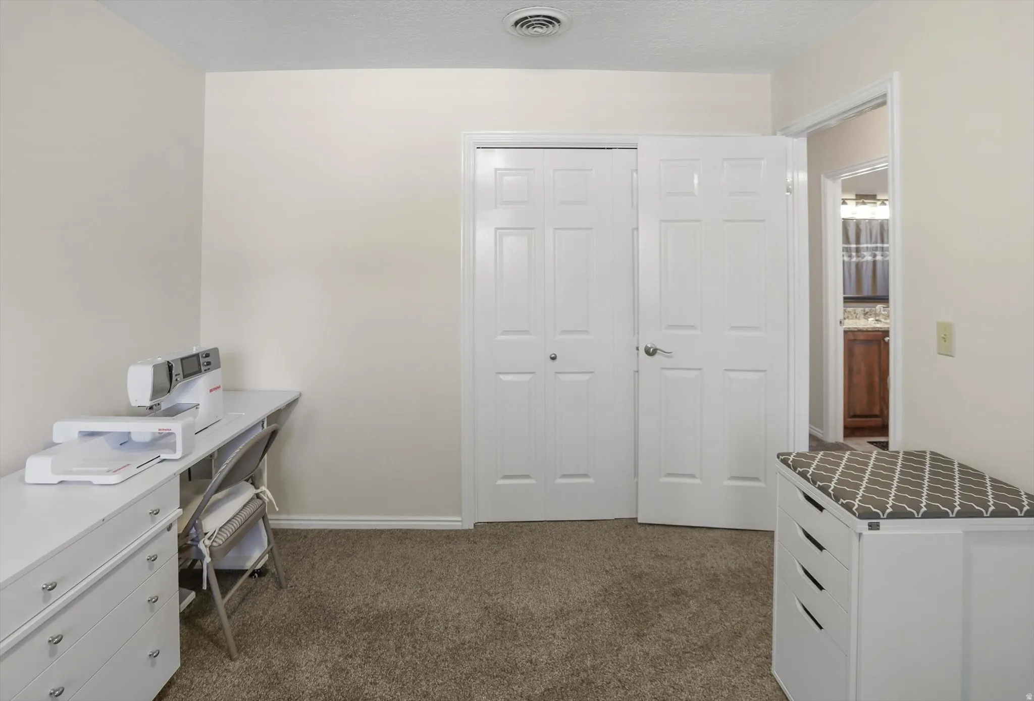 Carpeted room with light-toned walls, featuring a bi-fold closet door, a paneled interior door, and a ceiling-mounted air vent