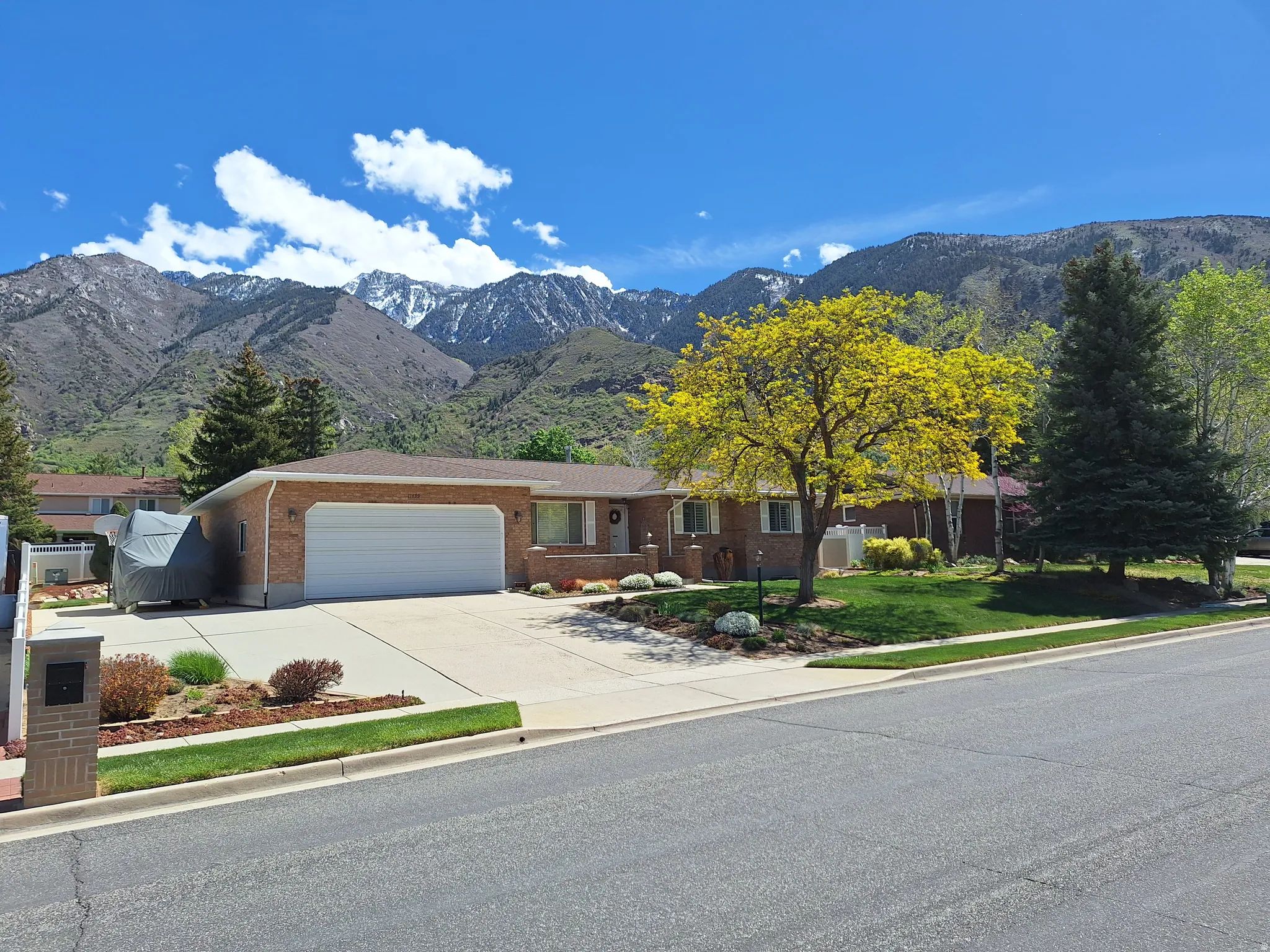 Brick-clad single-story residence featuring an attached two-car garage, mature landscaping, and a paved driveway