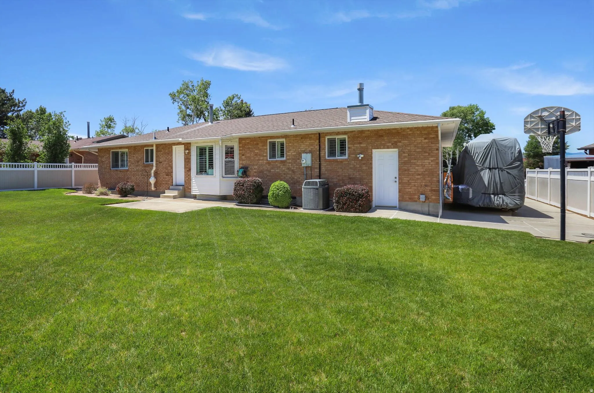 Brick exterior residence with a spacious lawn, multiple windows, a white vinyl fence, and an extended concrete pad