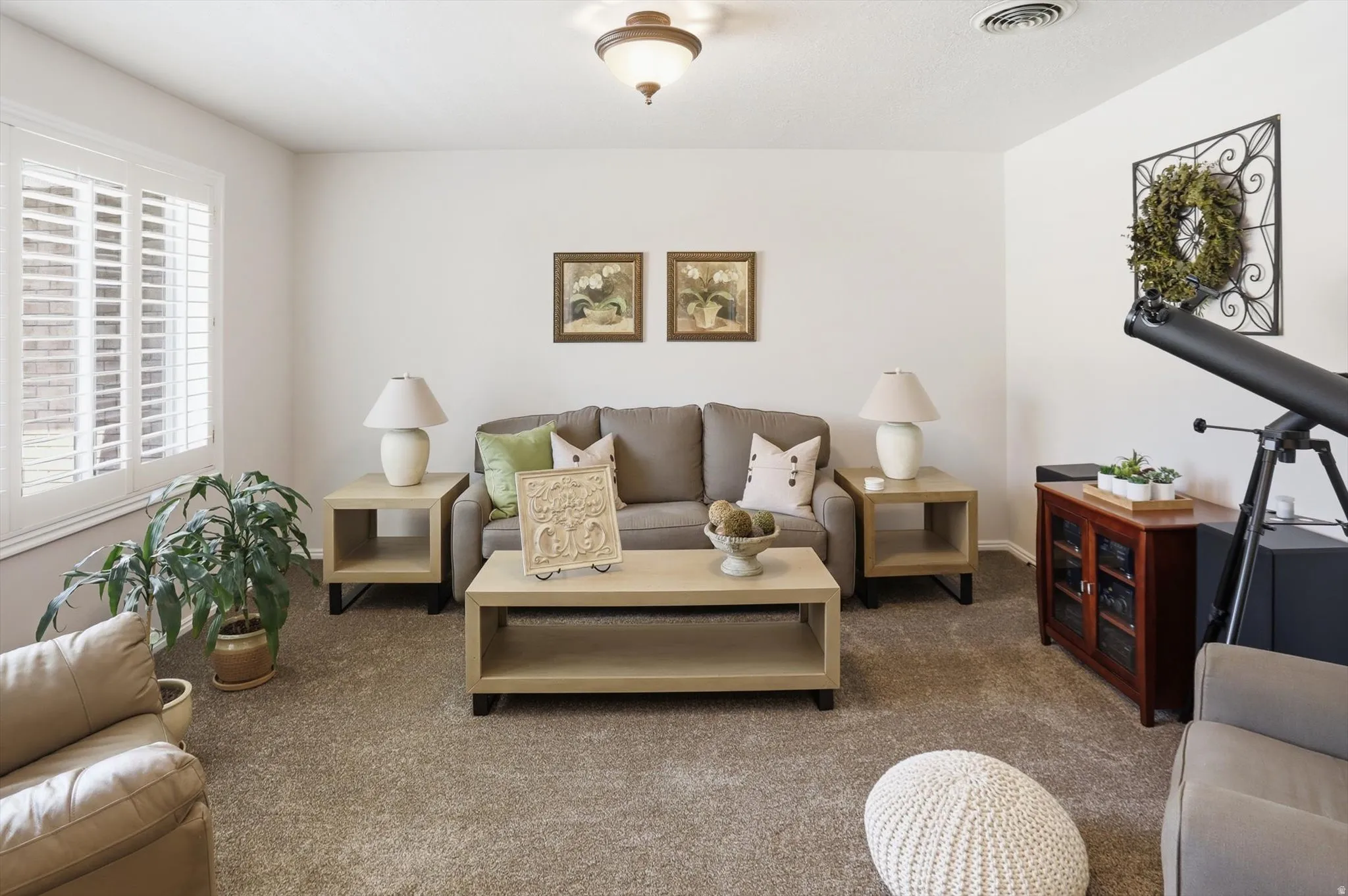 Living area featuring neutral wall tones, plush carpeting, a large window with white plantation shutters, and a ceiling-mounted light fixture