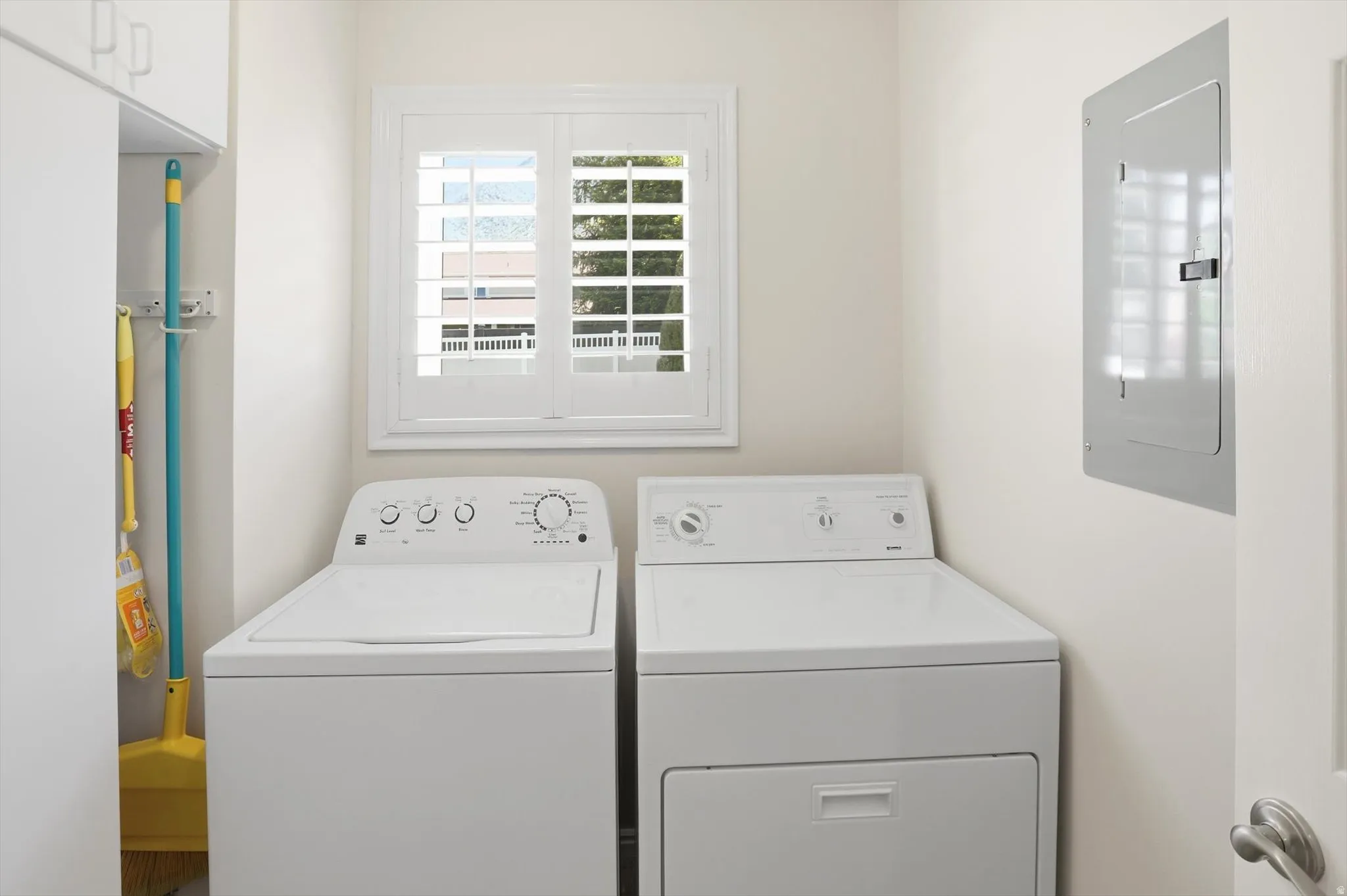 Dedicated laundry space featuring a white window with plantation shutters, a utility closet with shelving, and light-colored walls