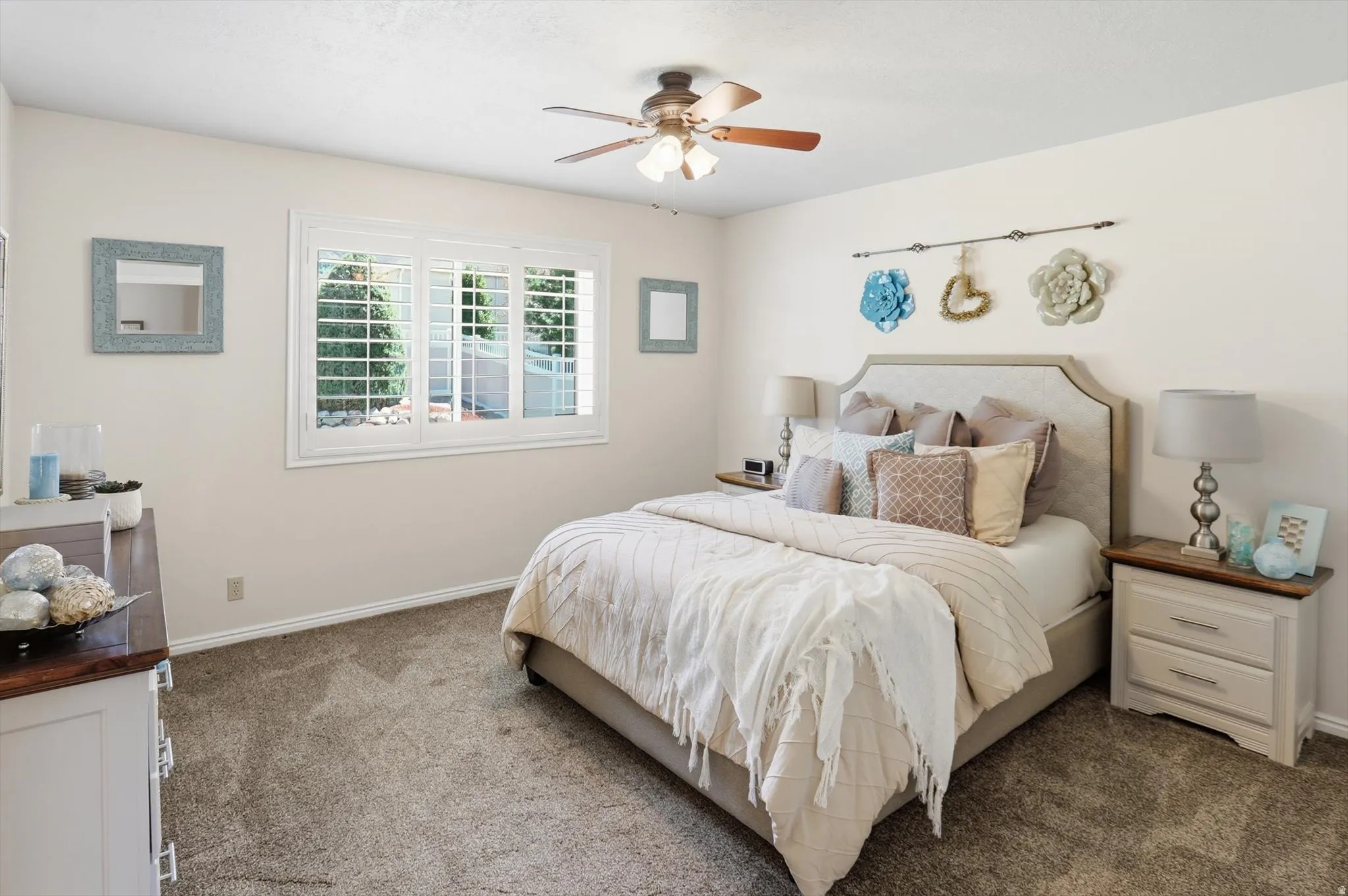 Bright bedroom featuring a ceiling fan with light fixture, plantation shutters, and soft wall-to-wall carpeting