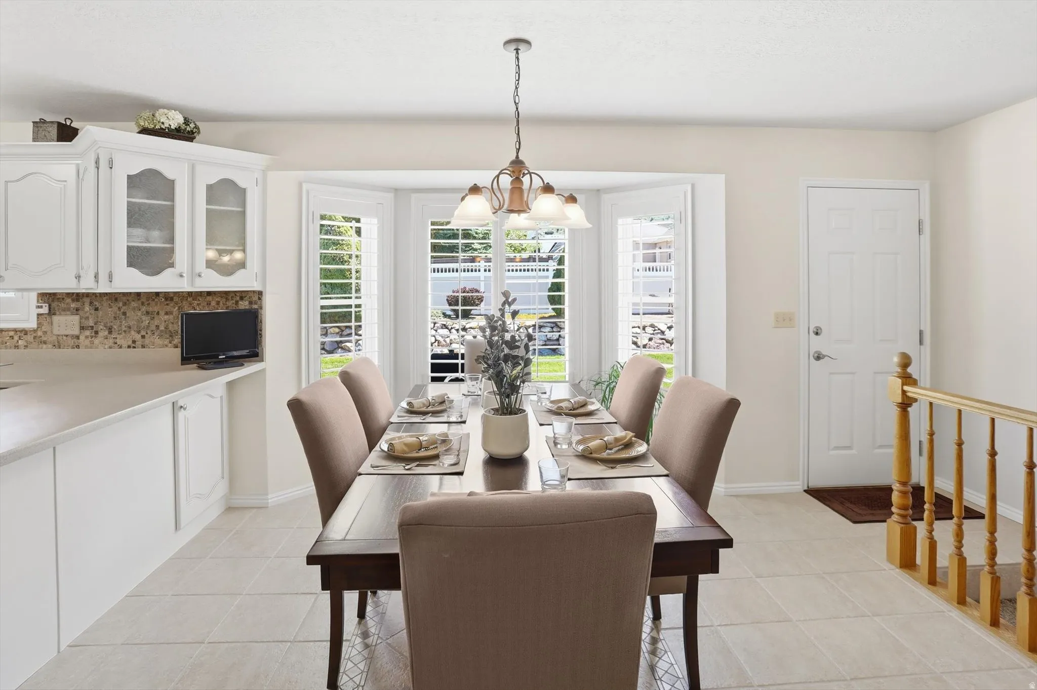 Dining area featuring a bay window with plantation shutters, tile flooring, and a chandelier