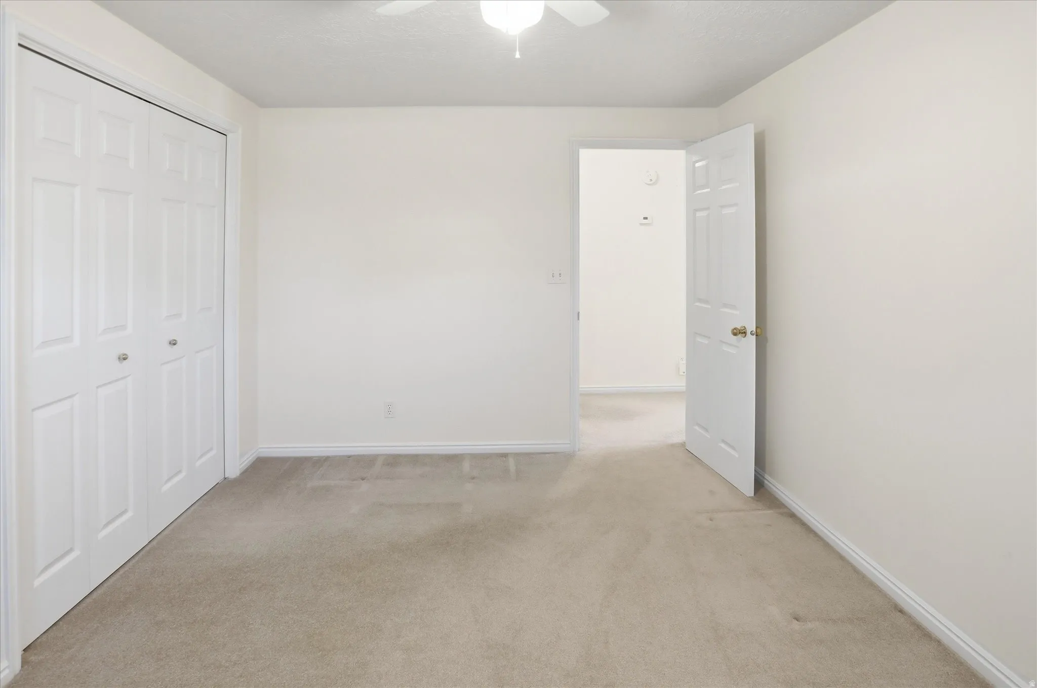 Light-toned carpeting in a neutral-painted room featuring a bi-fold closet door and white trim