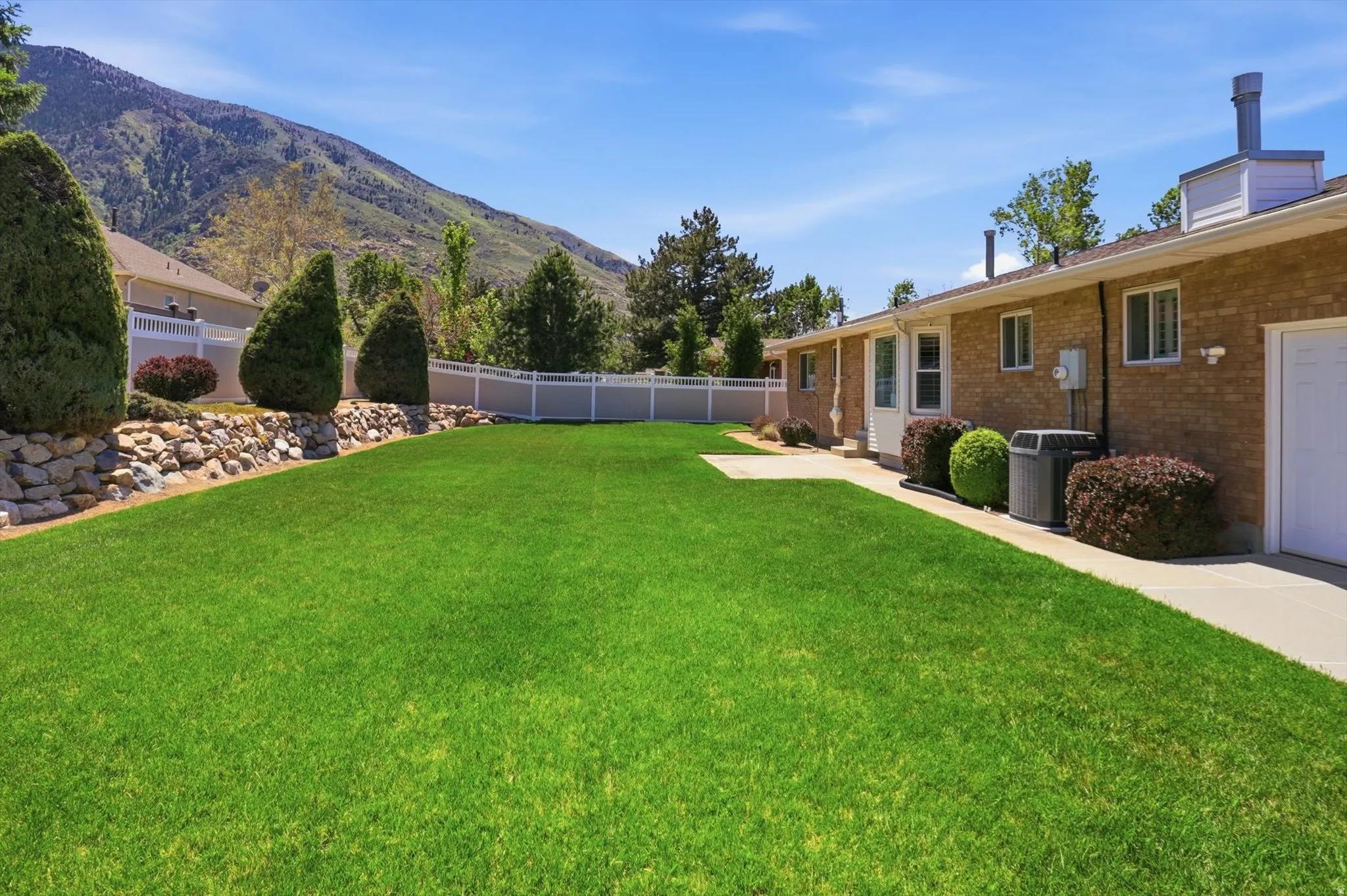 Expansive backyard featuring a manicured lawn, stone retaining wall, and mature landscaping