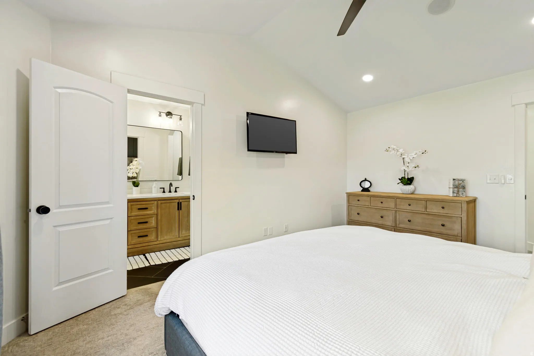 Vaulted ceiling bedroom with light-colored carpet flooring, recessed lighting and private bathroom.