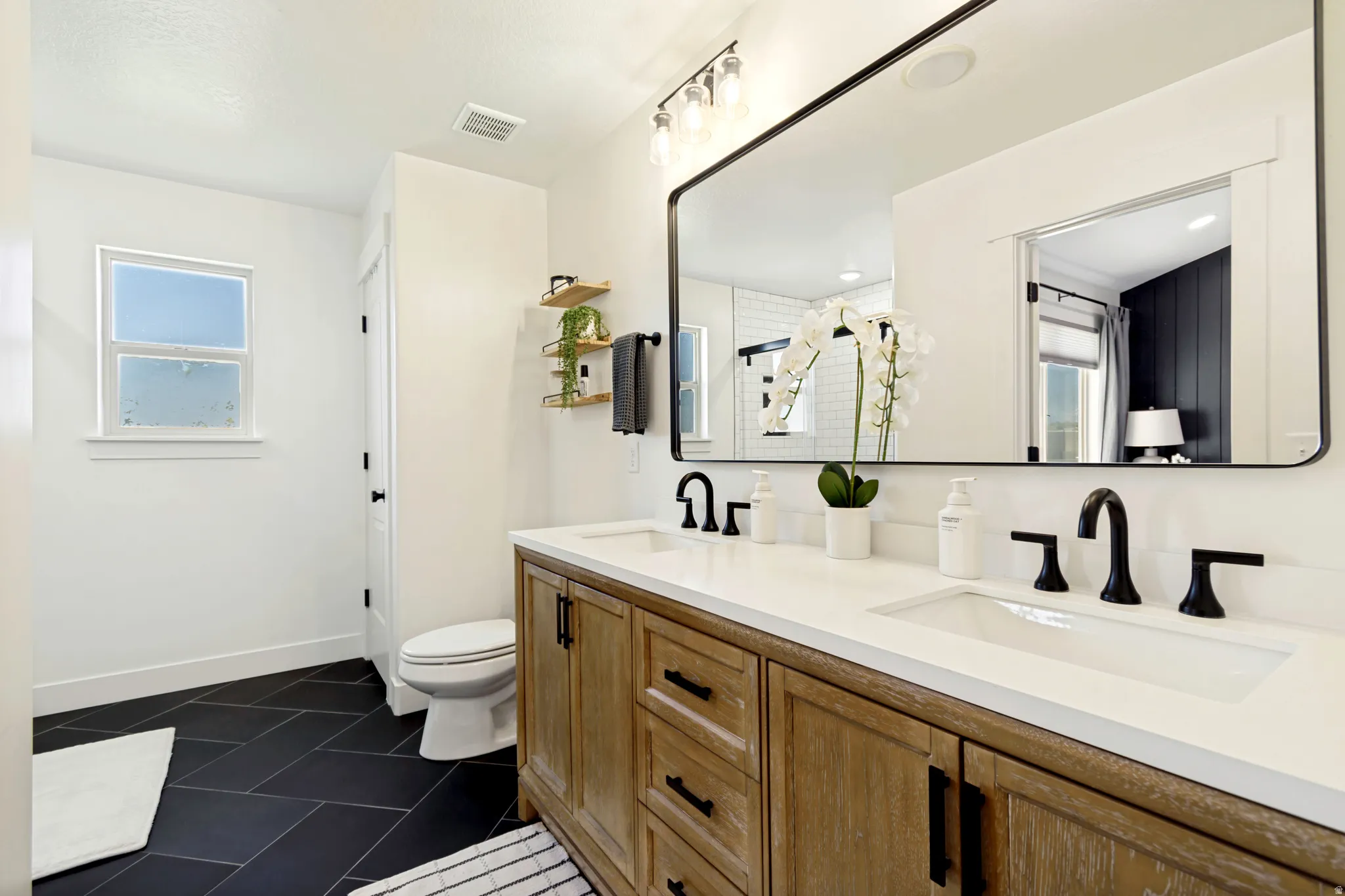 Contemporary bathroom featuring a double vanity with light wood-finish cabinetry and white countertops.