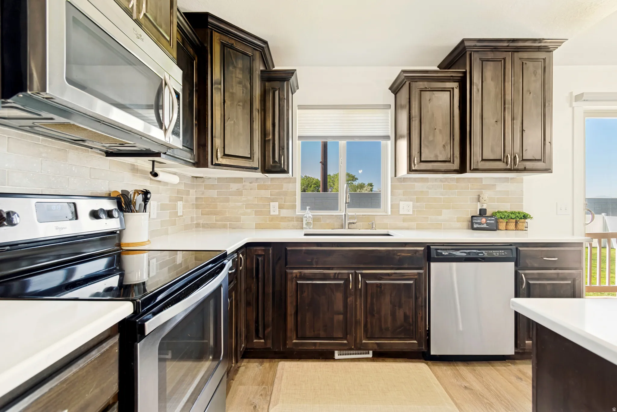 Kitchen featuring dark wood-finish cabinetry, light-toned tiled backsplash, stainless steel appliances, and white countertops.