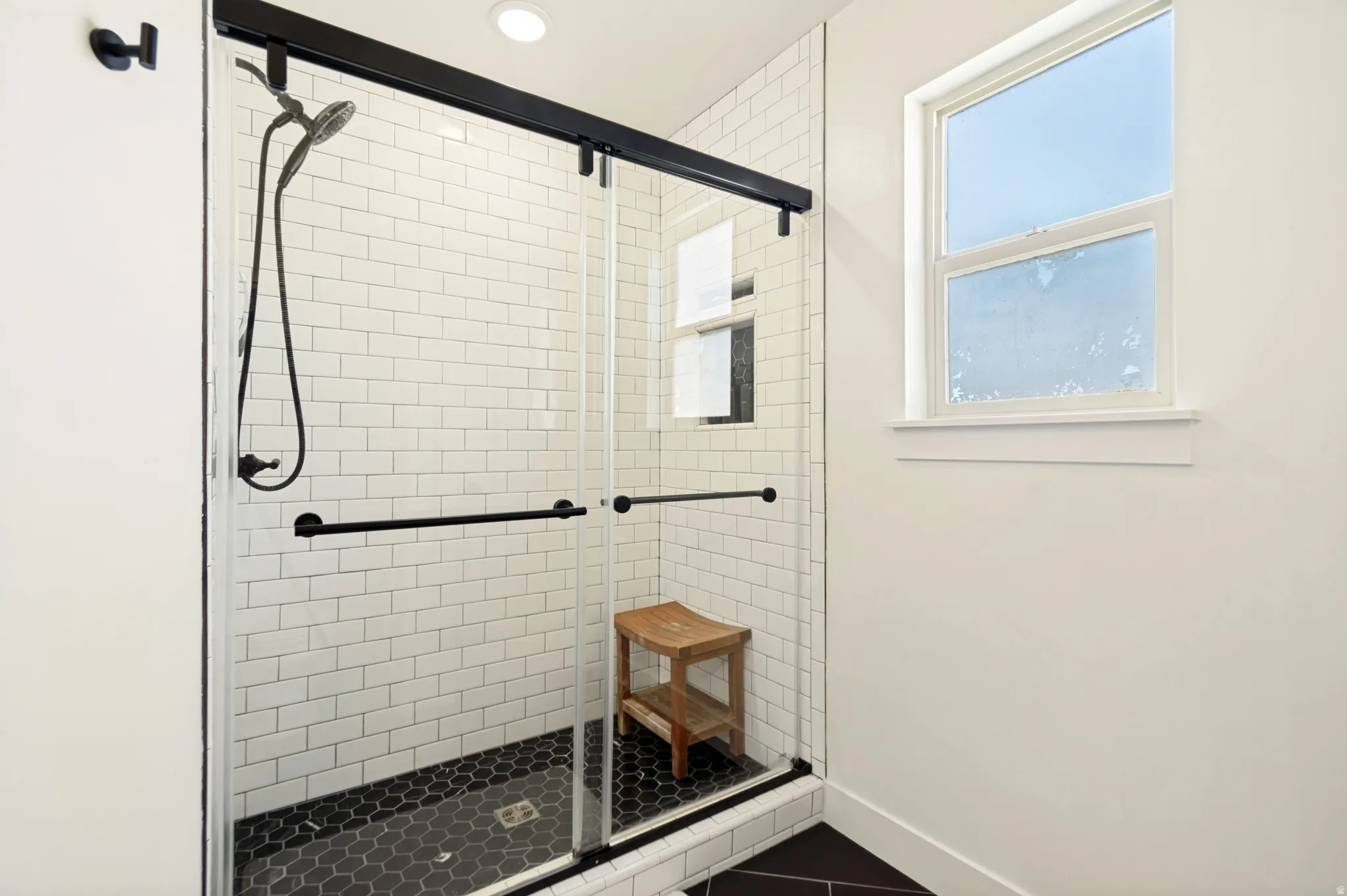 Large walk-in shower with clear glass enclosure, black hardware, white subway tile surround, and black hexagonal floor tile.