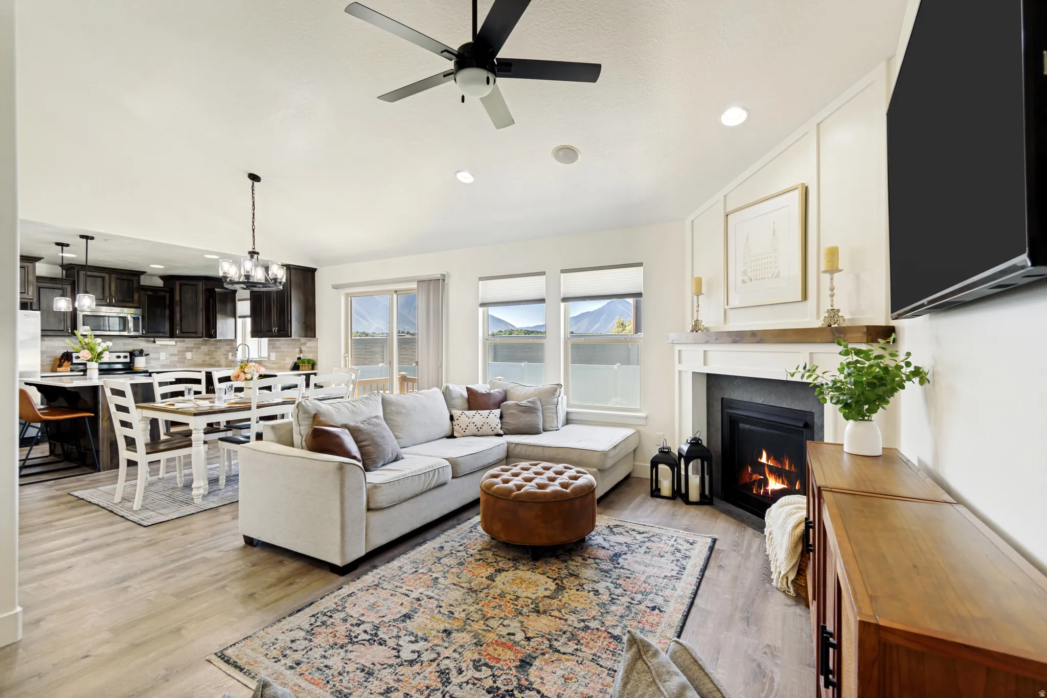 Open-concept living space featuring wood-finish flooring, a contemporary fireplace with a wooden mantel, and a ceiling fan.