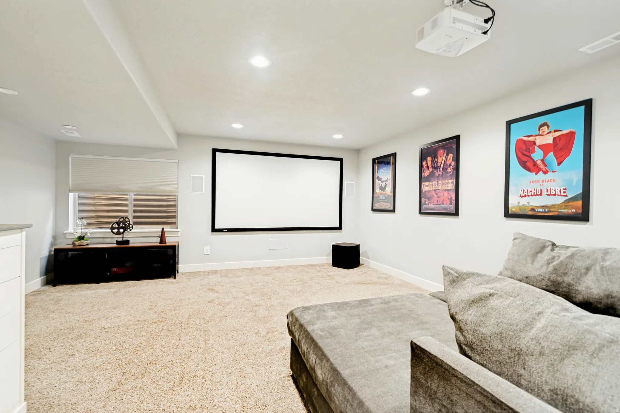 Dedicated media room featuring a large projection screen, mounted projector, recessed lighting, and neutral carpeting.