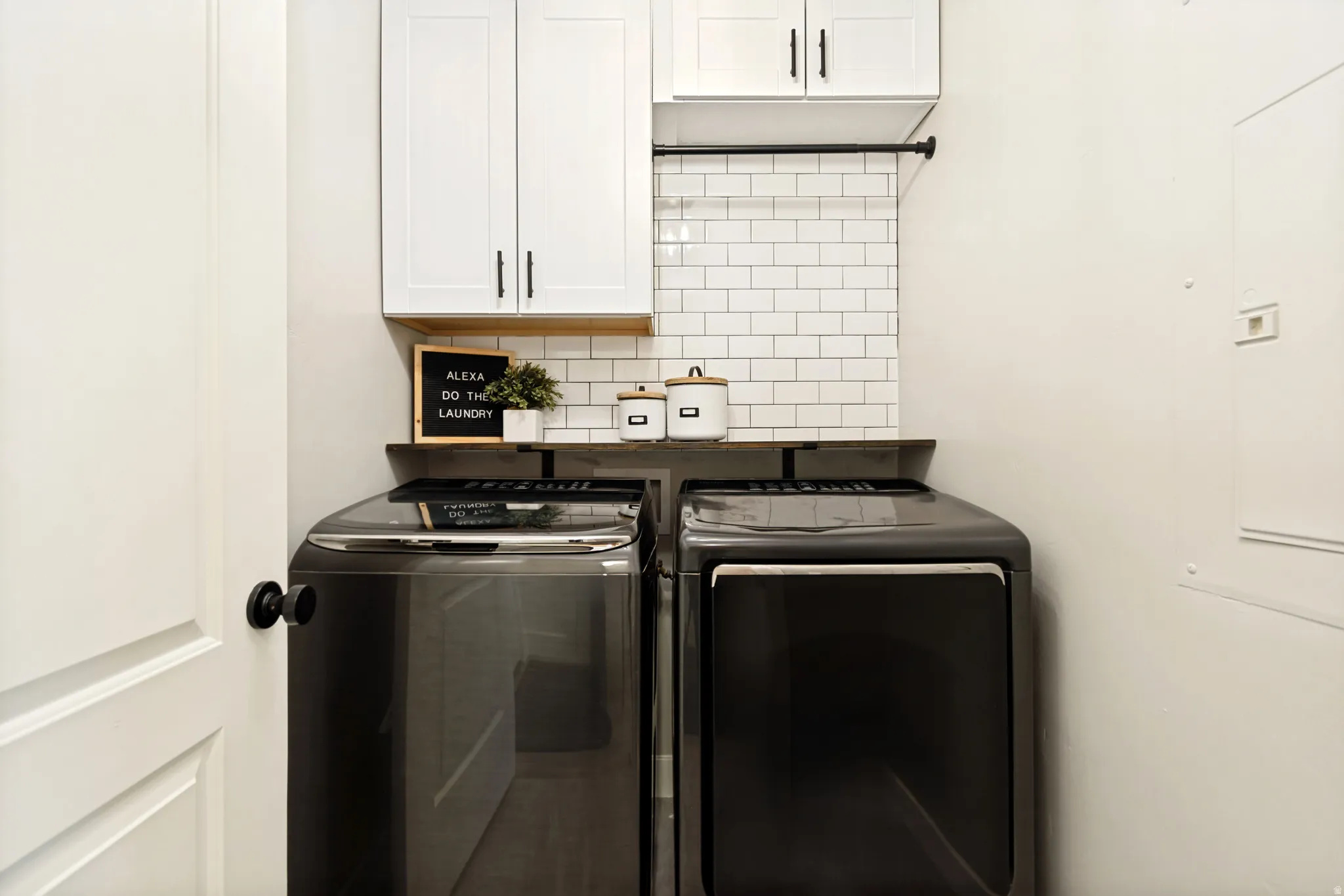 Utility area featuring white subway tile backsplash, a dark wood-finish shelf, and white cabinetry with dark hardware.