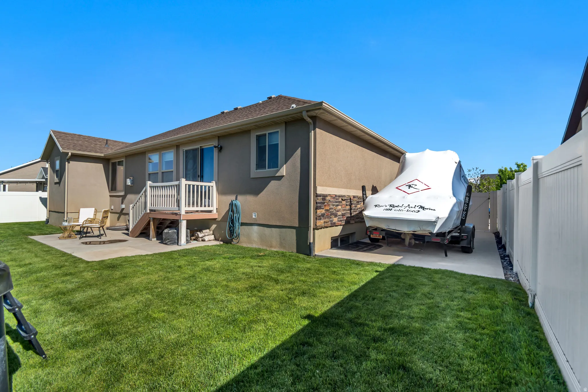 Expansive backyard featuring a concrete patio, a wooden deck with railing, and a private side yard with a concrete pad.