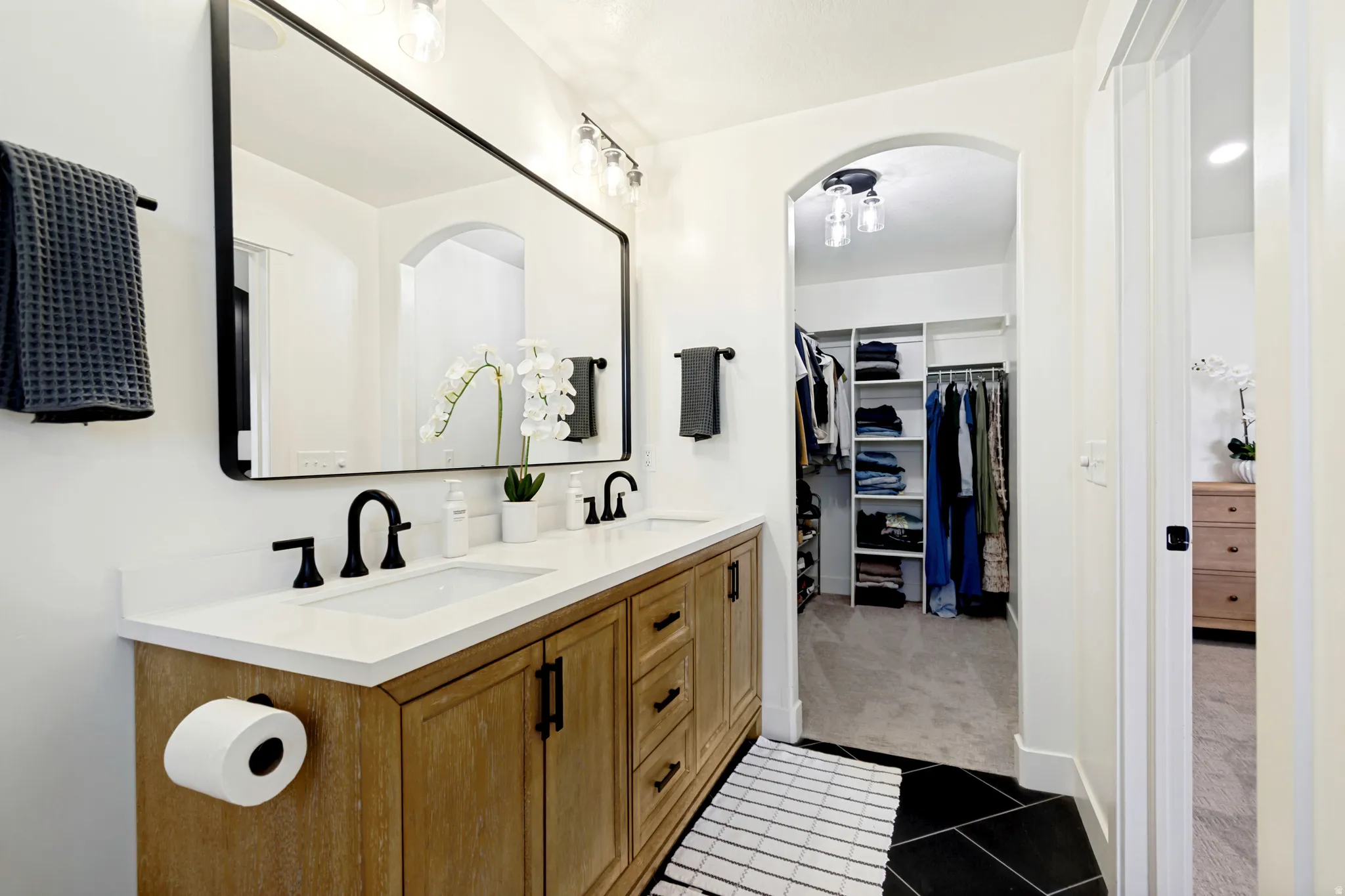 Dual vanity with white countertop, matte black fixtures, and wood-finish cabinetry.