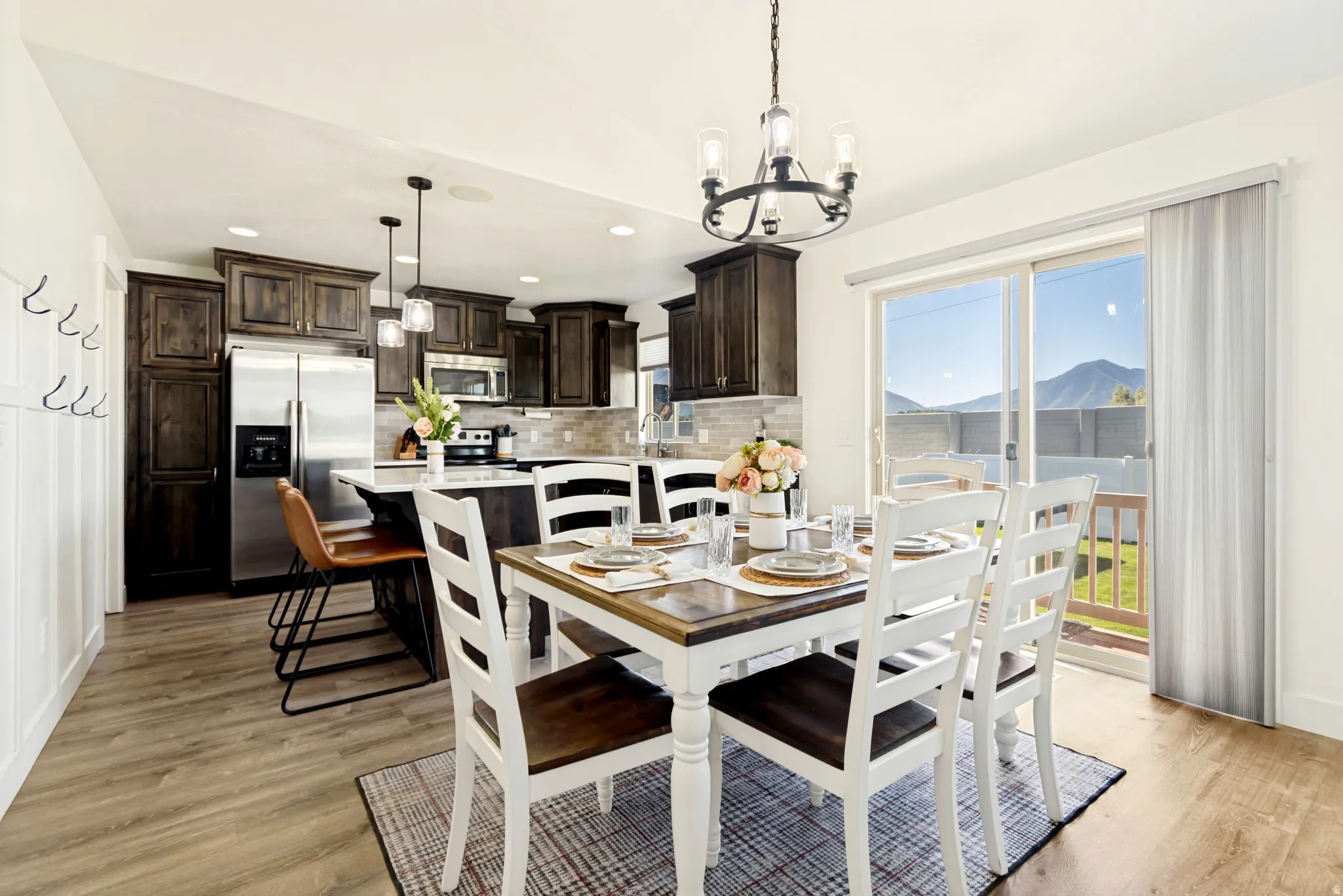 Open-concept dining area featuring wood-finish flooring, a contemporary chandelier, and direct patio access through sliding glass doors.