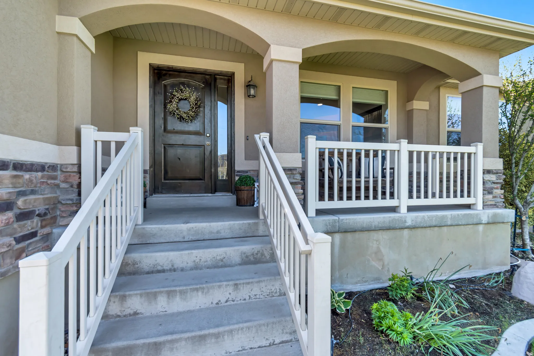 Inviting front entry featuring a cute covered porch, white railings, a dark wood-finish entry door, and a built-in outdoor light fixture.