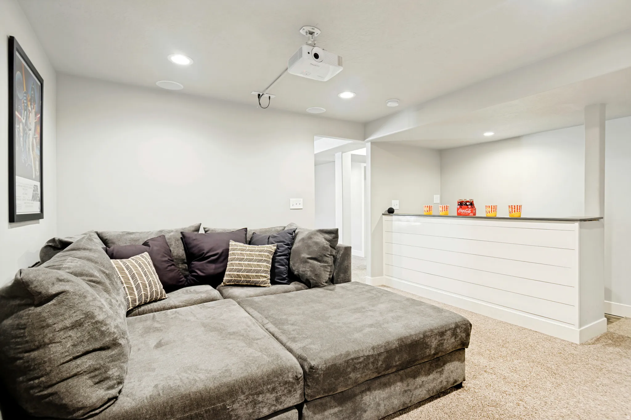 Recessed ceiling lighting illuminates a media area featuring a ceiling-mounted projector and integrated ceiling speakers.