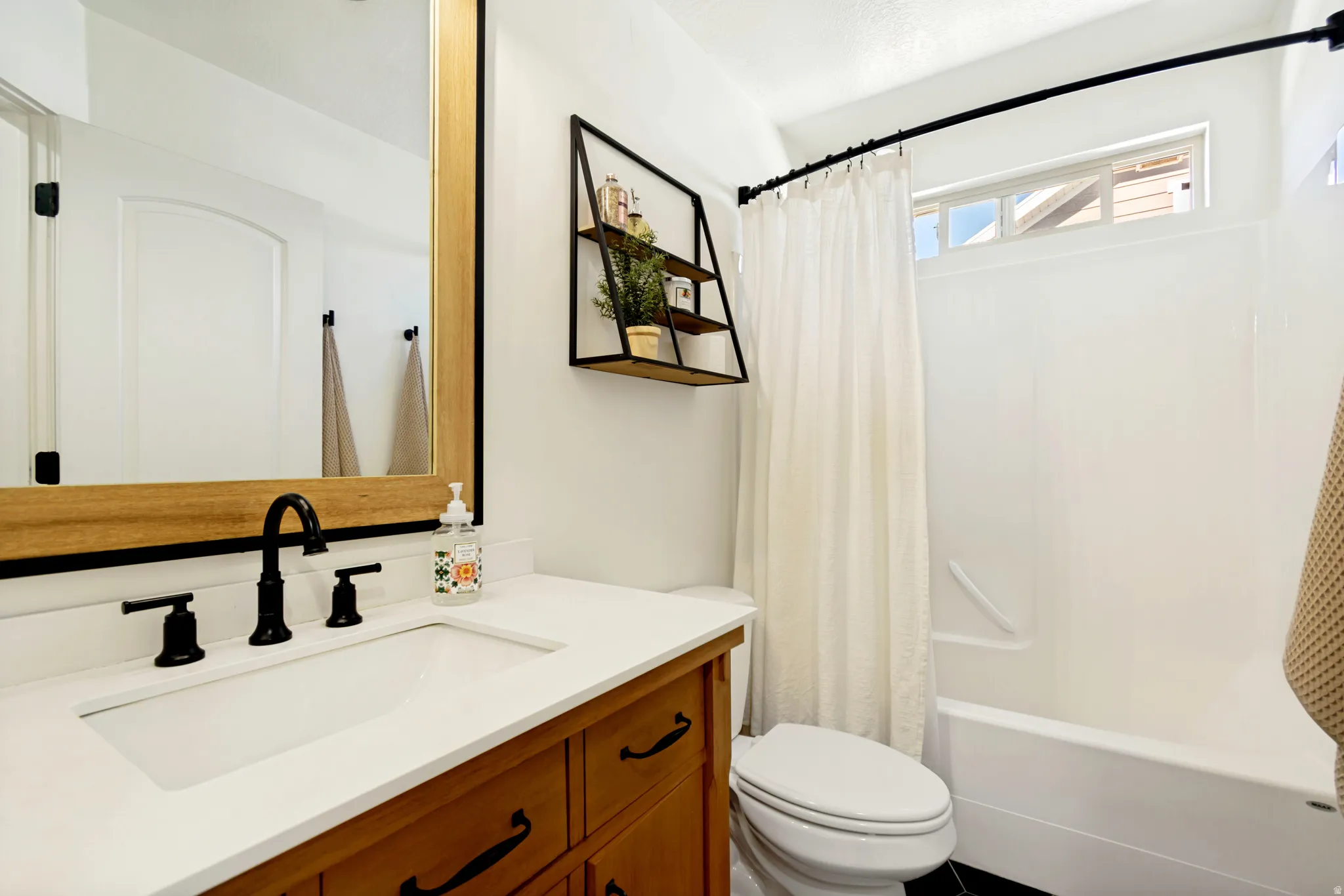 Bathroom featuring a wood-finish vanity with a white countertop and integrated sink, a large mirror with wood and black framing, and a shower/tub combination with a white surround.
