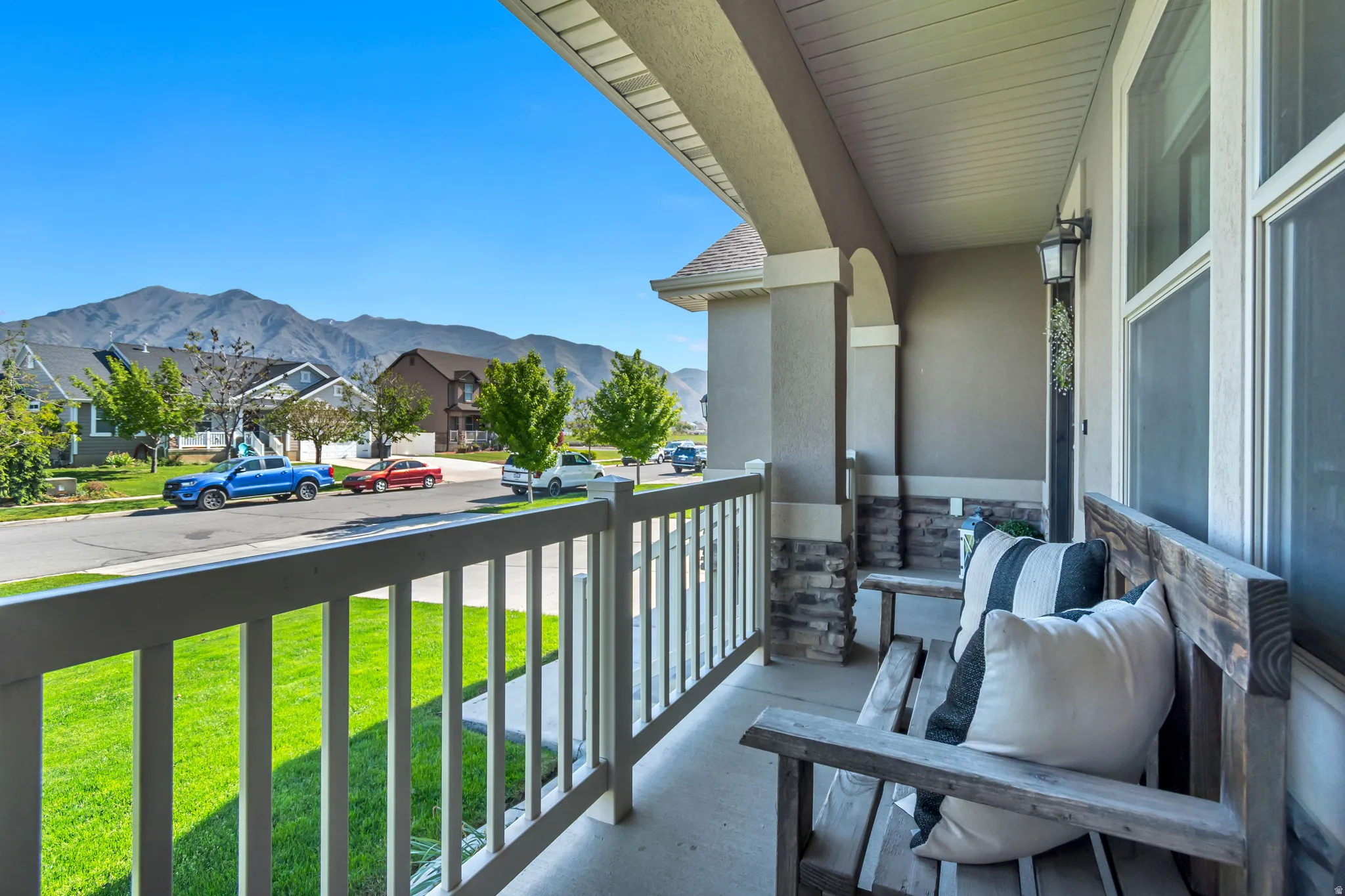 Covered front porch featuring robust columns with stone accents, a durable railing, and a clear mountain backdrop.