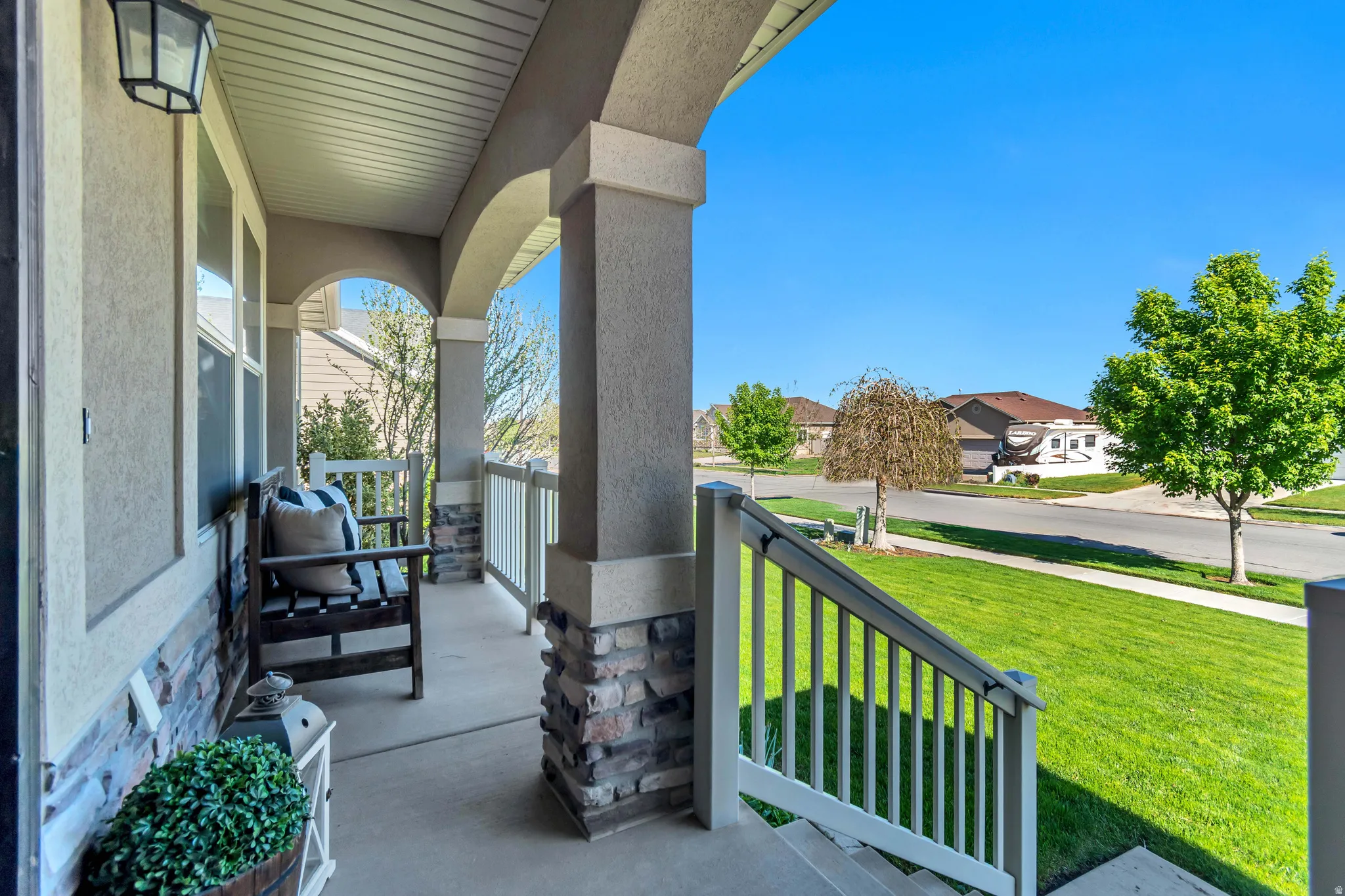 Arched front porch with stone veneer accents, concrete flooring, and white railing.