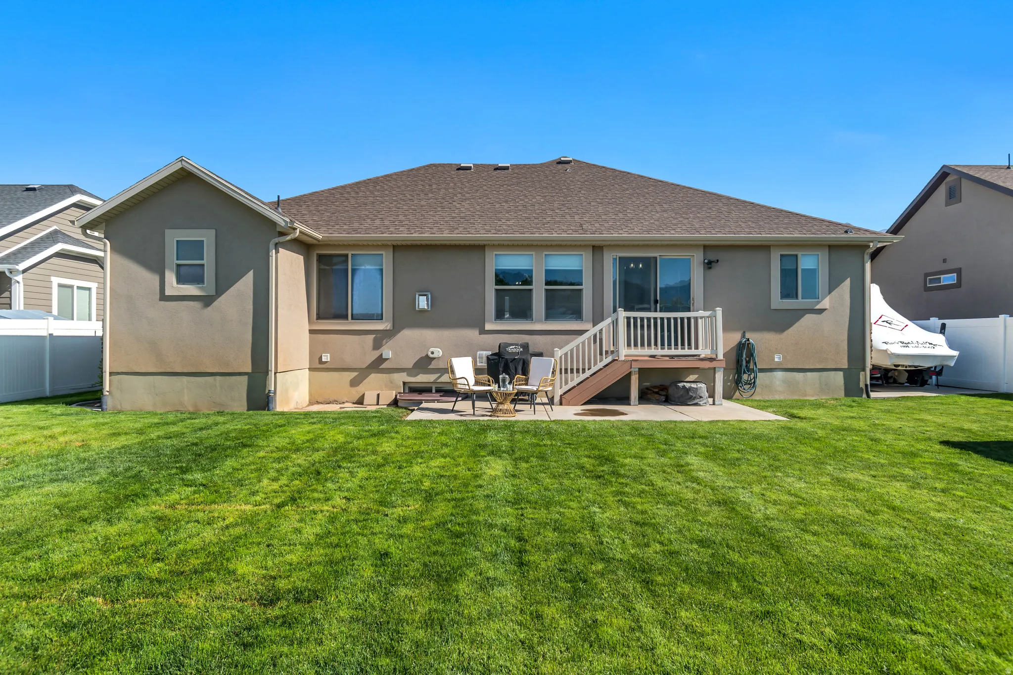 Spacious backyard featuring a manicured lawn, an elevated deck with white railings, a ground-level concrete patio, and a stucco exterior