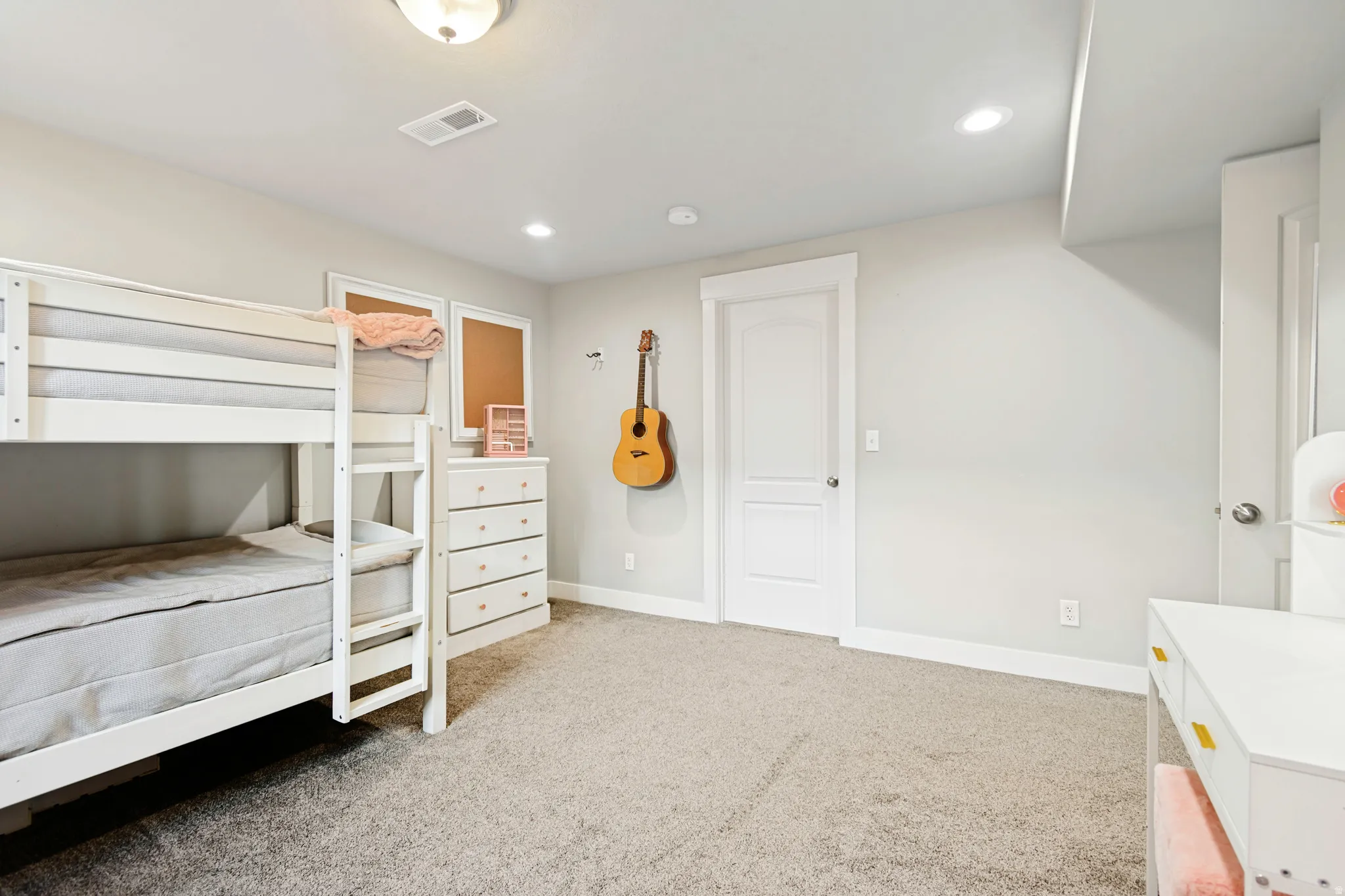 Spacious room featuring neutral carpeting, light gray walls, white trim, recessed lighting, and a white paneled door.