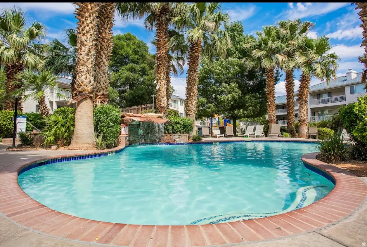 Community swimming pool with a decorative waterfall feature, surrounded by mature palm trees and lush landscaping