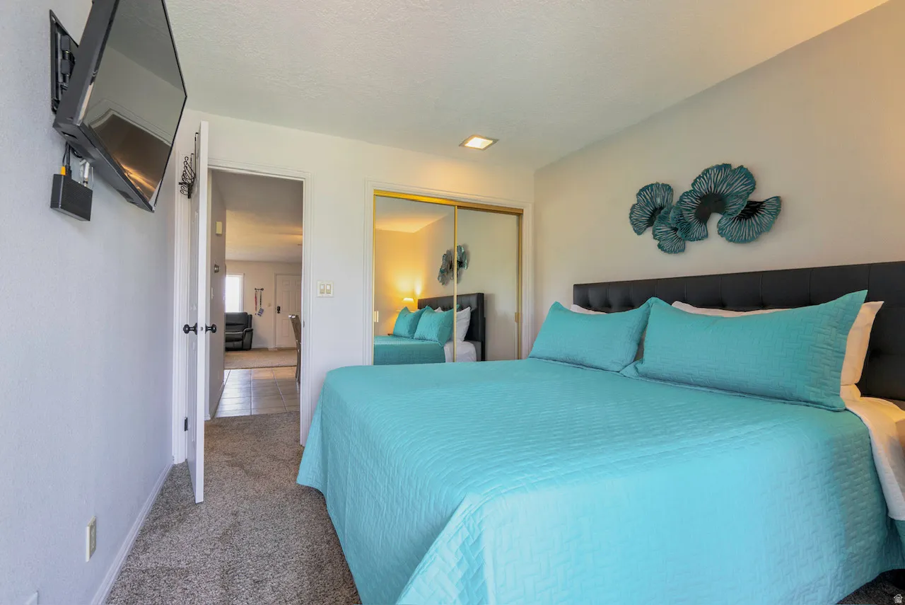 Carpeted room featuring a built-in wall-mounted television, recessed lighting, and a closet with mirrored sliding doors
