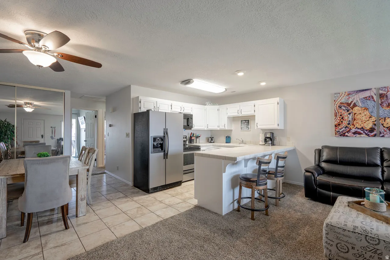 Open-concept living area featuring a kitchen with white cabinetry and stainless steel appliances, a breakfast bar with seating, tile flooring in the kitchen and dining areas, and a ceiling fan in the dining space