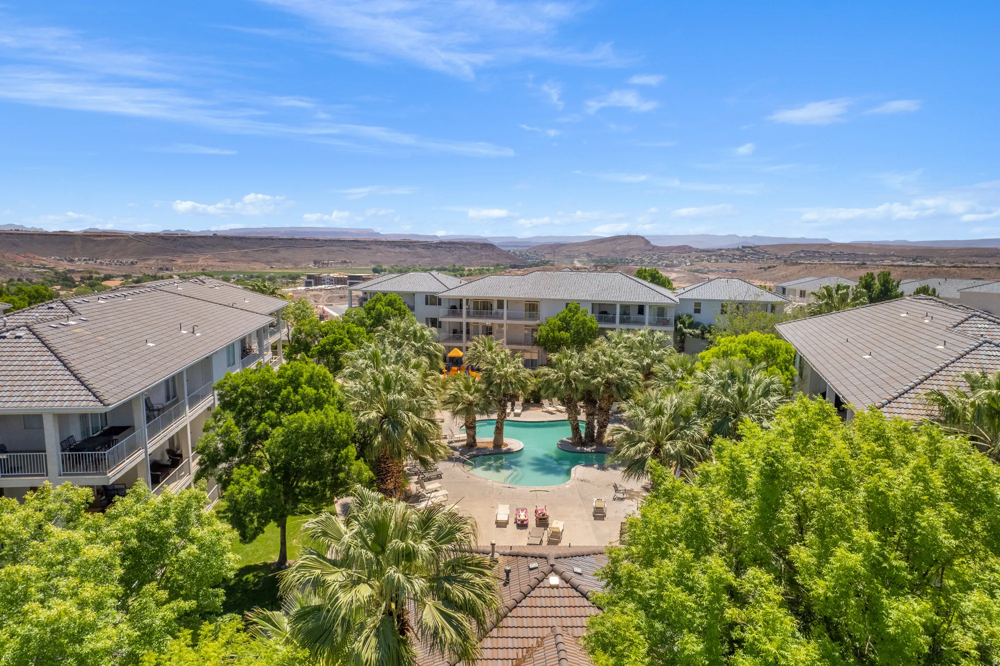 Resort-style pool area surrounded by lush palm trees and mature foliage, featuring multiple lounge chairs and an inviting water feature