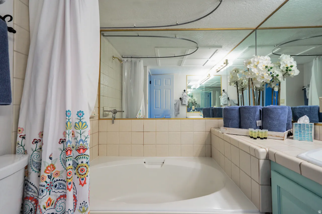 Built-in soaking tub with surrounding ceramic tile, illuminated by overhead lighting and a large wall-mounted mirror