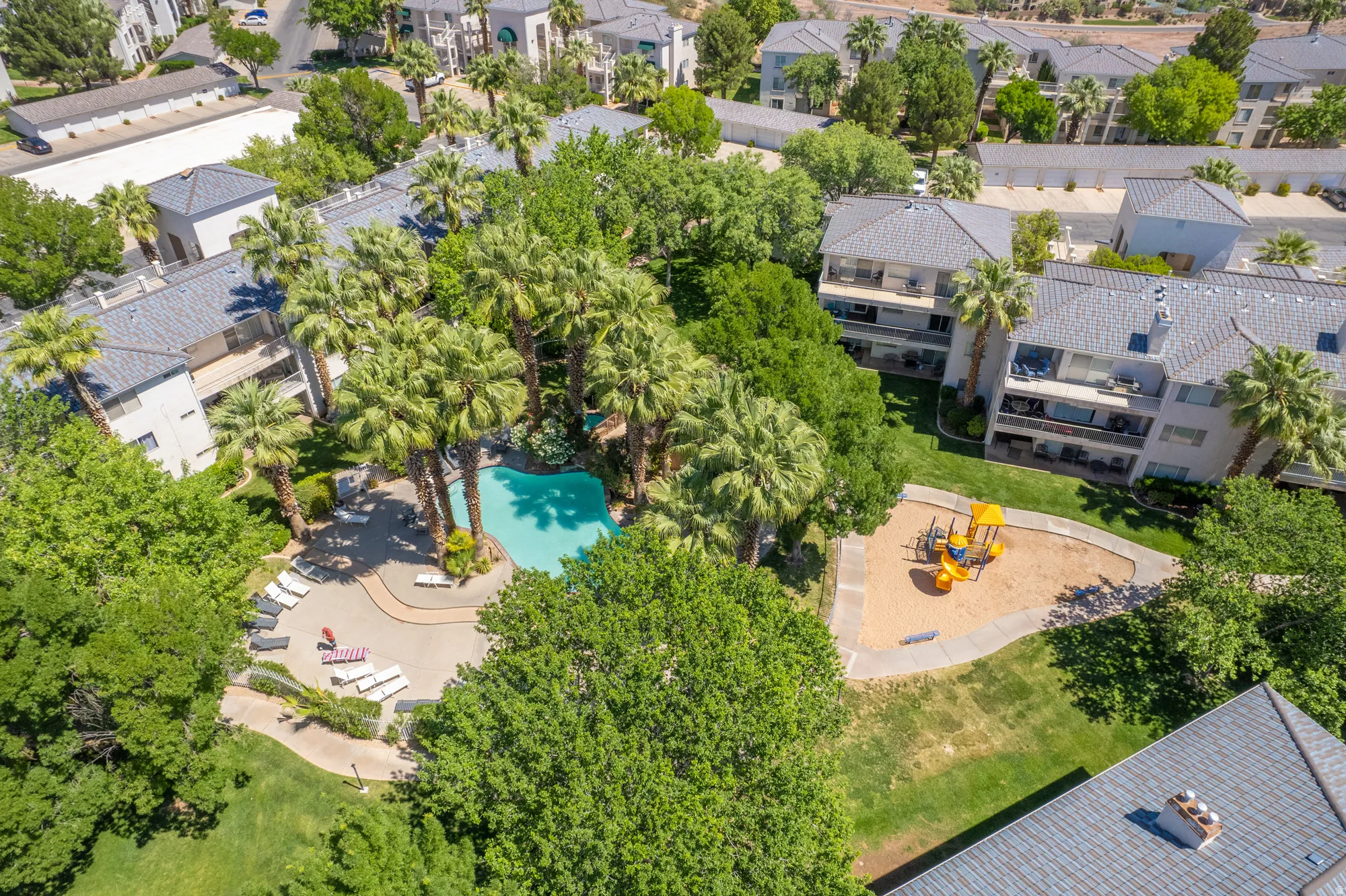 Resort-style pool area surrounded by lush palm trees, featuring a spacious patio with multiple lounge chairs
