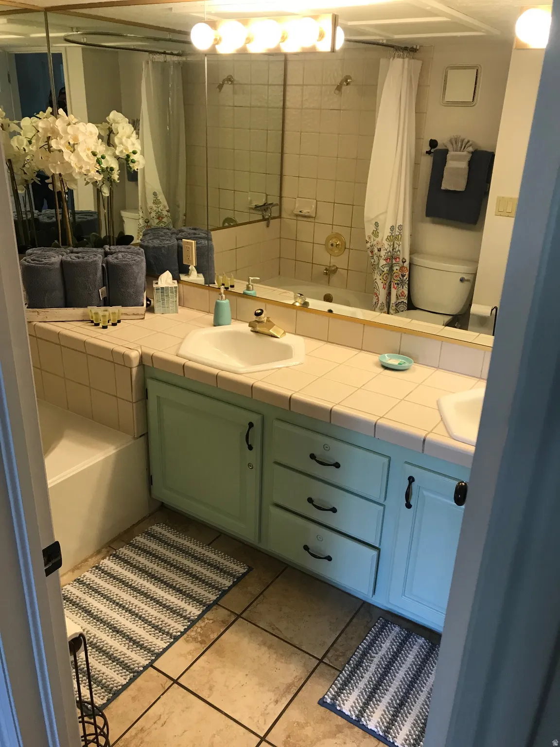 Bathroom featuring a double vanity with light blue cabinetry, tiled countertops, and dual sinks