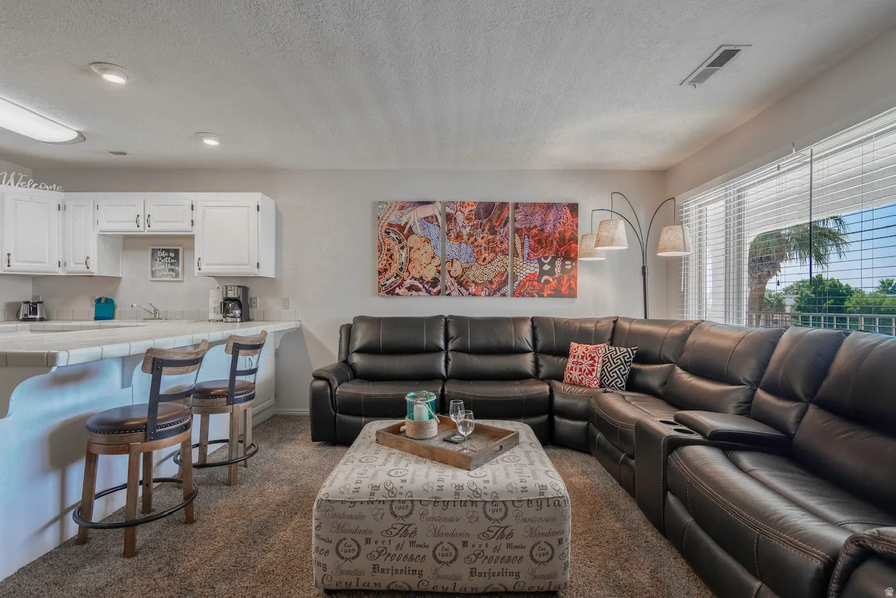 Open-concept living space with a kitchen bar, white cabinetry, and large windows