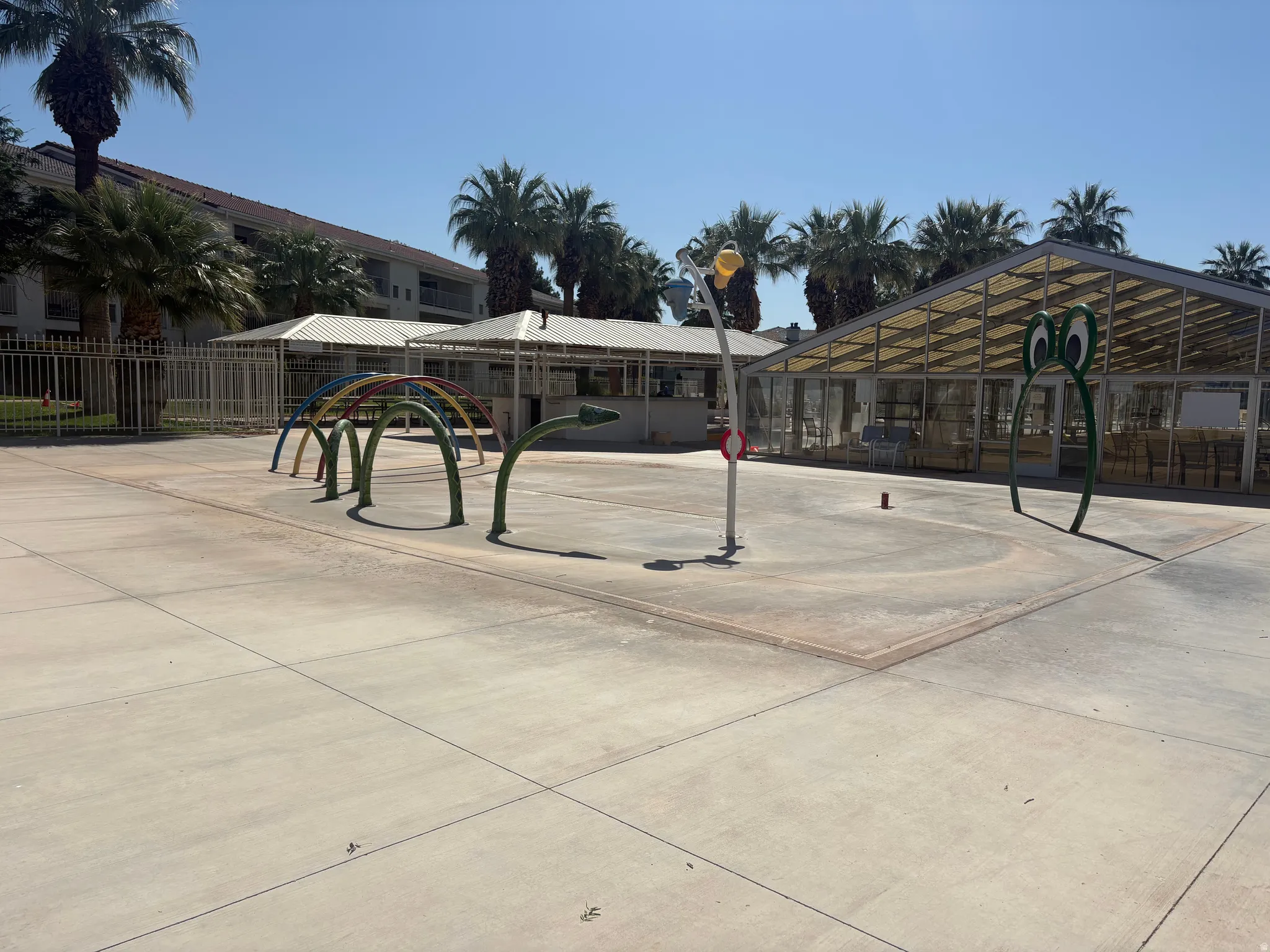 Concrete splash pad area featuring multiple water play structures, including a rainbow arch and a whimsical green arch
