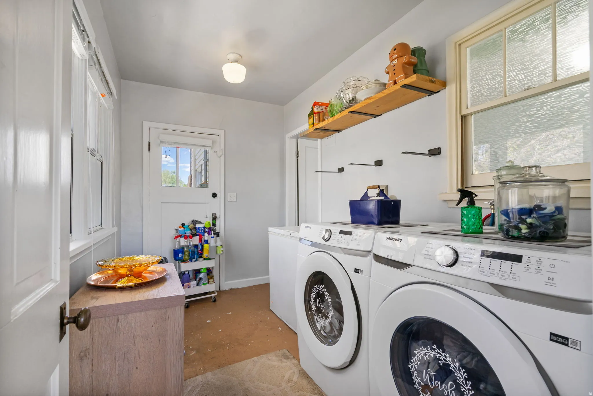 Utility room featuring multiple windows, a wood-finish floating shelf, a white paneled door with glass insert, and a globe light fixture