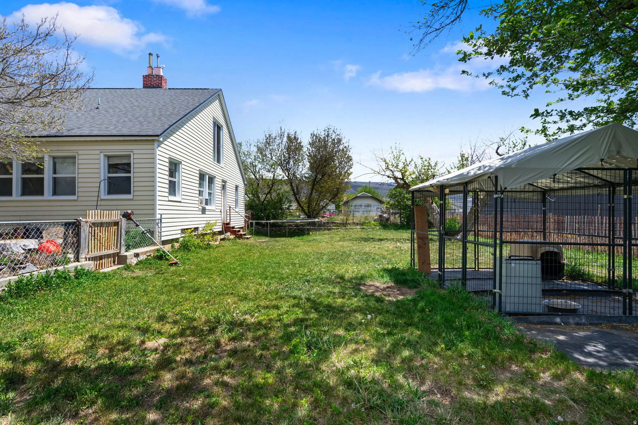 Spacious grassy yard featuring a chain-link fence, established trees, and a covered outdoor enclosure