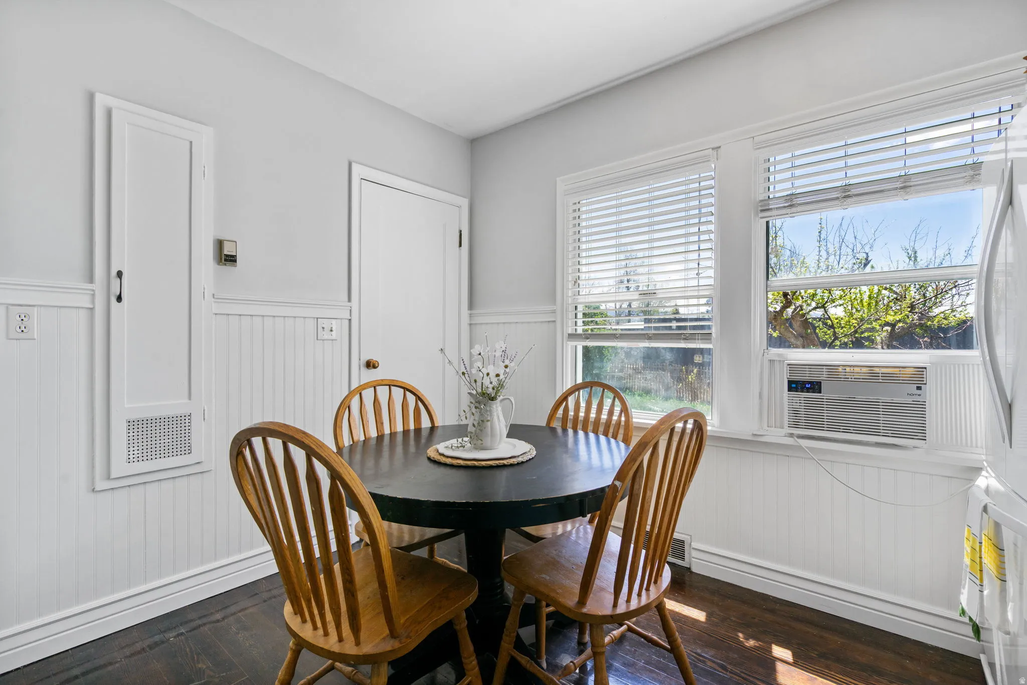 White beadboard wainscoting and trim, wood-finish flooring, and multiple windows with blinds