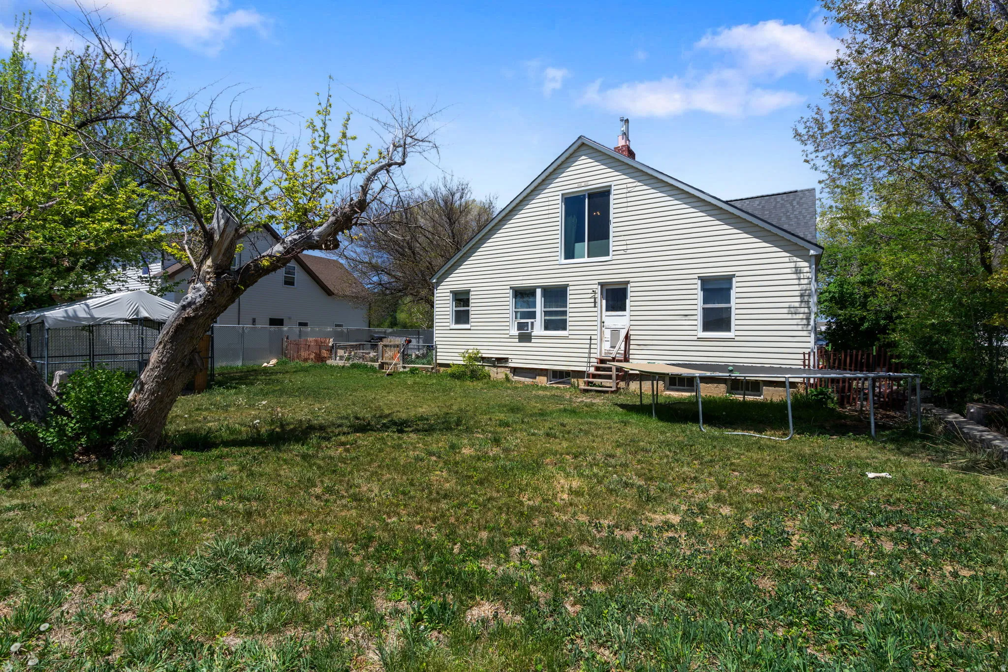 Expansive backyard featuring a mature tree, a privacy fence, and a two-story home exterior with light-colored siding and multiple windows