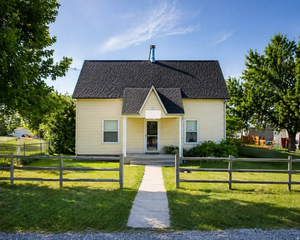 Charming single-story residence featuring light yellow siding and a dark shingled roof