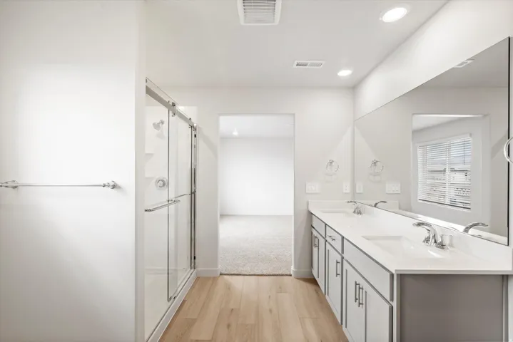 Bathroom featuring wood-finish flooring, a double vanity with an integrated sink and chrome fixtures, a full-width mirror, and a glass-enclosed shower with a sliding door