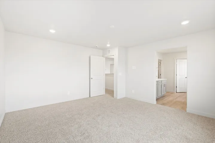 Spacious room featuring neutral carpeting, recessed lighting, white walls, and a white door with panel detailing