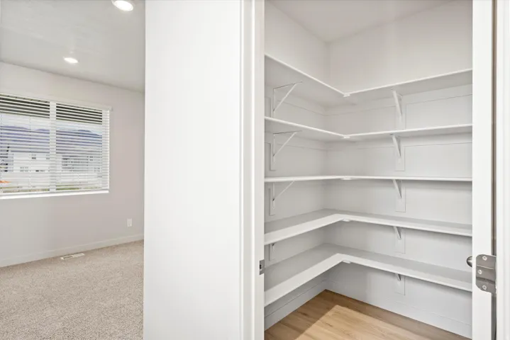 Spacious walk-in pantry featuring multiple white shelving units and wood-finish flooring