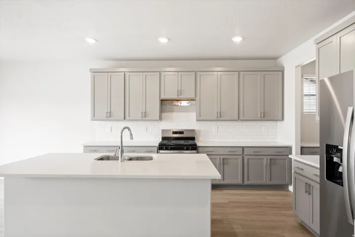 Contemporary kitchen featuring light gray cabinetry, stainless steel appliances, a white subway tile backsplash, and a large island with an integrated sink