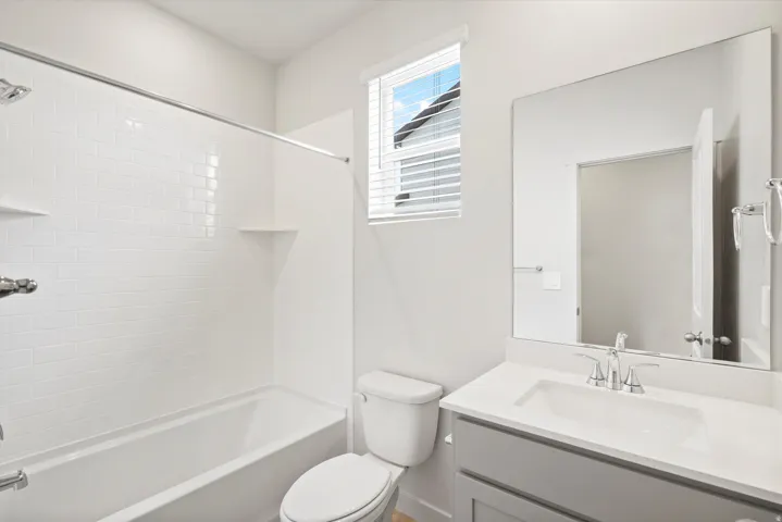 Bright bathroom featuring a white subway tile tub surround with integrated shelving, a dual-flush toilet, and a vanity with a white countertop, undermount sink, and chrome fixtures