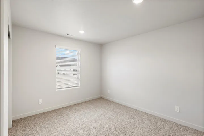 Bright room featuring light-colored walls, recessed ceiling lighting, a window with horizontal blinds, and neutral-toned carpeting