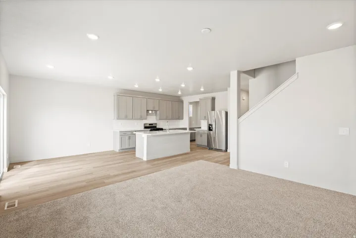 Open-concept living space with a contemporary kitchen, light wood-finish flooring, recessed lighting, white perimeter walls, and a staircase