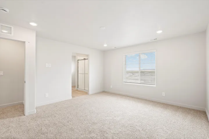 Spacious room featuring neutral carpeting, white walls, and a large window with horizontal blinds
