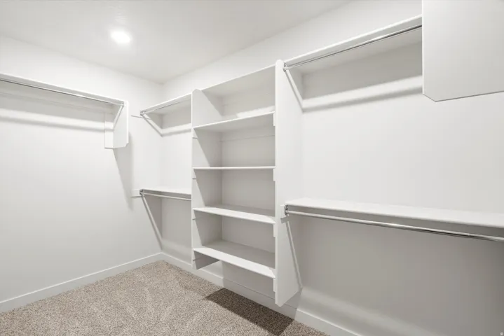 Walk-in closet featuring built-in shelving, multiple hanging rods, white walls, recessed lighting, and carpet flooring